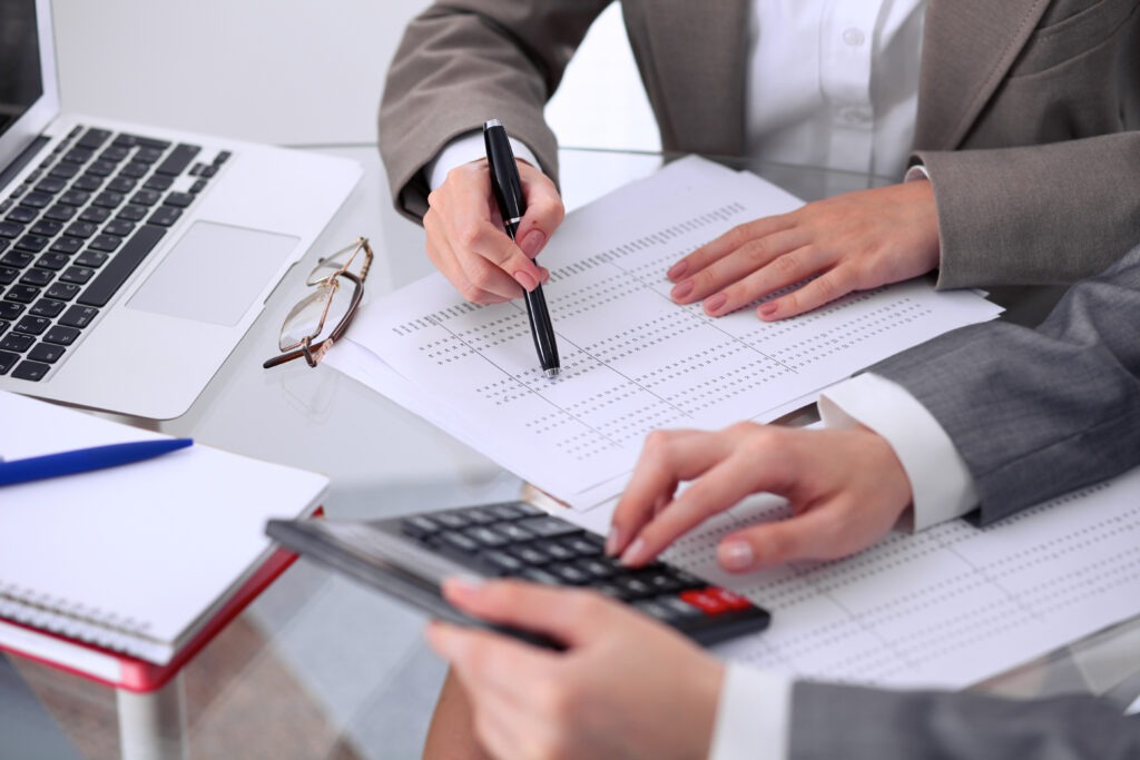 Two female accountants counting on calculator income for tax form completion hands closeup.